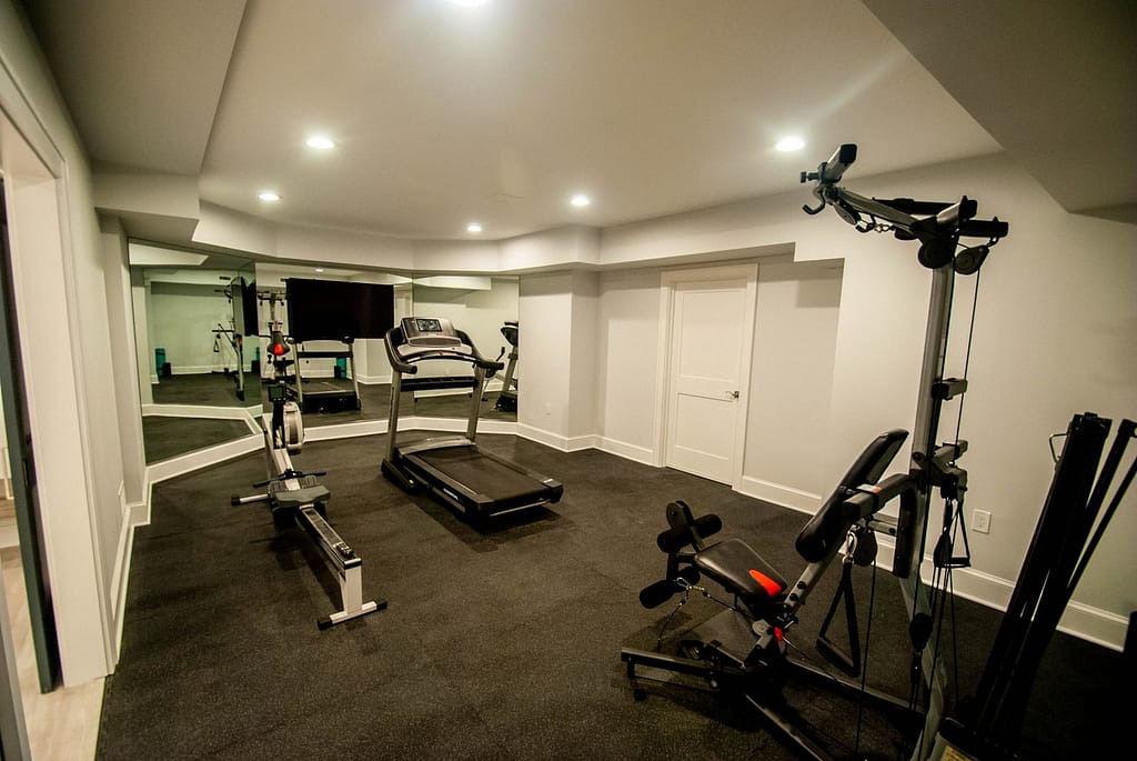 A basement gym with a large open space surrounded by mirrors and hand selected gym equipment